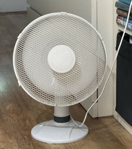 Valkoinen pöytätuuletin lattialla puhaltamassa ilmaa.